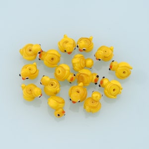 May include: A collection of yellow glass beads shaped like ducklings. The beads have orange beaks and black eyes.