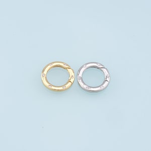 May include: Two round metal clasps with small clear stones set around the edge. One clasp is gold and the other is silver.