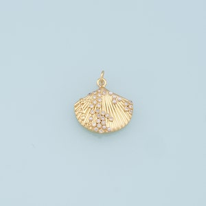 May include: Gold seashell charm with a textured surface and small white pearls. The charm is decorated with tiny clear crystals.