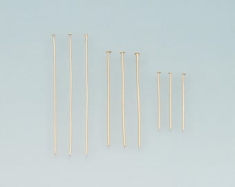 May include: A collection of gold-colored head pins of varying lengths, arranged on a light blue surface. The pins have a small, flat head and a straight, slender shaft. Ideal for jewelry making and crafting.