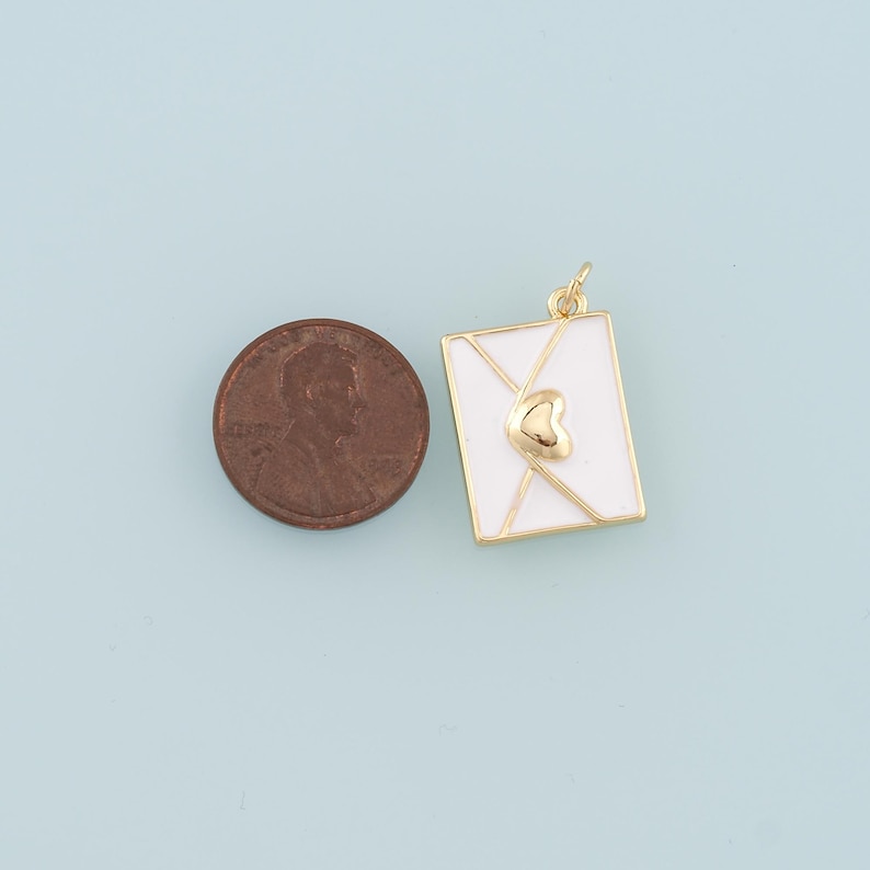 May include: Gold-tone charm in the shape of a white envelope with a gold heart on the front. The charm is about the size of a UK penny.