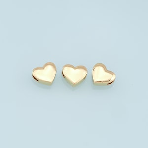 May include: Three gold heart-shaped charms with a smooth, shiny finish. The charms have a small hole at the top for attaching to a necklace or bracelet.