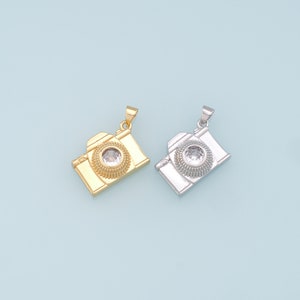 May include: Two camera-shaped pendants, one gold and one silver, with a clear crystal in the center of each.