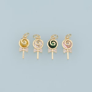 May include: Four gold-colored lollipop charms with different colored centers: yellow, clear, green, and pink. Each charm has a bow-shaped base with clear stones and a loop at the top for hanging. The background is a light blue.