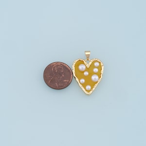 May include: A gold heart-shaped pendant with a yellow enamel fill and white pearl accents.