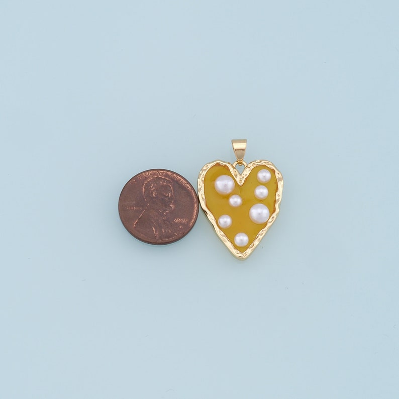 May include: A gold heart-shaped pendant with a yellow enamel fill and white pearl accents.