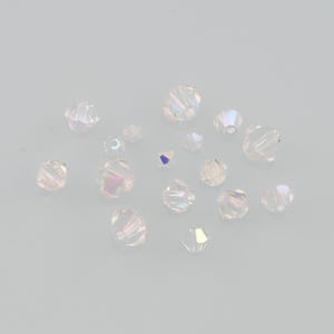 Puede incluir: Una colección de cuentas de cristal transparentes y facetadas con un brillo iridiscente. Las cuentas varían en tamaño y forma, reflejando la luz con un efecto arcoíris. Ideal para la fabricación de joyas o proyectos de manualidades.