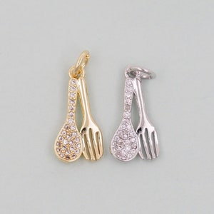 May include: Two charm pendants, one gold and one silver, each featuring a spoon and fork design with clear crystal embellishments.