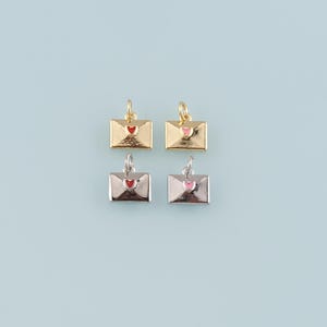 May include: Four small envelope charms in gold and silver tones, each with a heart detail. Two are gold with red and pink hearts, and two are silver with red and pink hearts. The charms have a small loop at the top for attaching to jewelry.