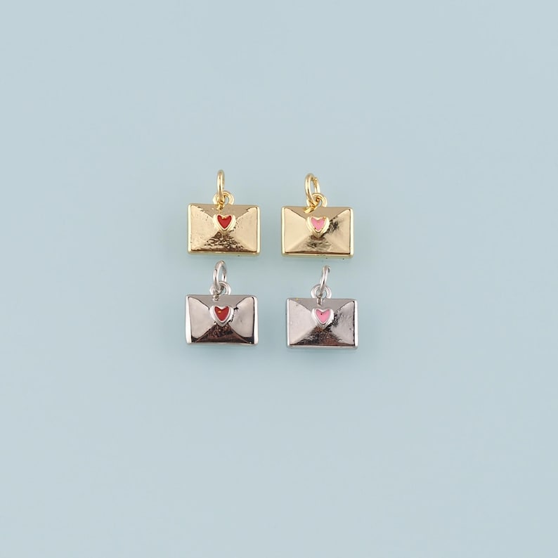 May include: Four small envelope charms in gold and silver tones, each with a heart detail. Two are gold with red and pink hearts, and two are silver with red and pink hearts. The charms have a small loop at the top for attaching to jewelry.