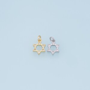 May include: Two silver charms in the shape of a Star of David with clear crystals around the edges. The charm on the left is gold and the charm on the right is silver.