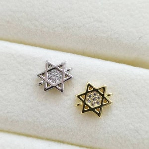 May include: Two silver and gold Star of David charms with clear crystal accents. The charms are in a white velvet box.