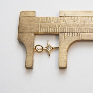 May include: A gold-toned star charm with a clear rhinestone in the center. The charm is measured with calipers, showing it is approximately 1.5 inches in length.