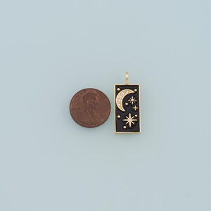 May include: Gold charm with a black enamel rectangle featuring a crescent moon and stars with white rhinestones. The charm is about the size of a US penny.
