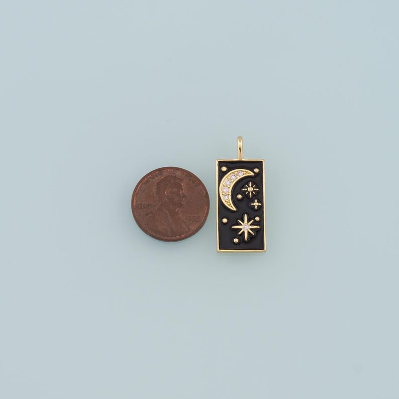May include: Gold charm with a black enamel rectangle featuring a crescent moon and stars with white rhinestones. The charm is about the size of a US penny.