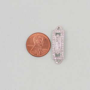 May include: Silver charm with a clear crystal border and a cutout image of the Virgin Mary inside. The charm is about the size of a UK penny.