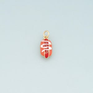 May include: A gold-colored charm in the shape of a hot dog. The charm features a red hot dog with white squiggles of sauce and red accents. The charm is suspended from a small gold loop.