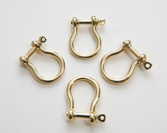 May include: Four gold-colored metal D-rings with a swiveling pin. The D-rings are arranged in a circle on a white background.