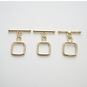 May include: Three gold-toned metal toggle clasps with square loop closures. Each clasp has a straight bar with two round ends.