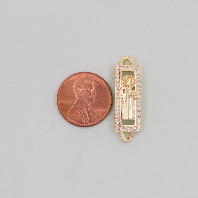 May include: Gold-toned charm with a clear crystal border, featuring a raised image of a saint. The charm is about the size of a UK penny.