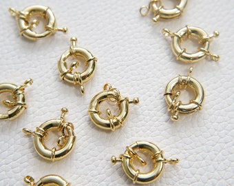 May include: Ten gold-toned metal lobster clasps, each with a circular design and two small loops. These clasps are commonly used for jewelry making.