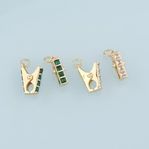 May include: Four gold-toned metal clasps with crystal accents. Each clasp has a different colored crystal: green, clear, and white.