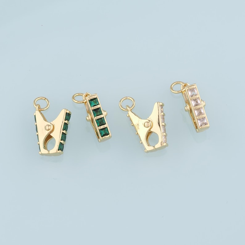 May include: Four gold-toned metal clasps with crystal accents. Each clasp has a different colored crystal: green, clear, and white.