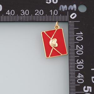 May include: Gold charm in the shape of a red envelope with a gold heart inside. The charm is approximately 2 cm wide.