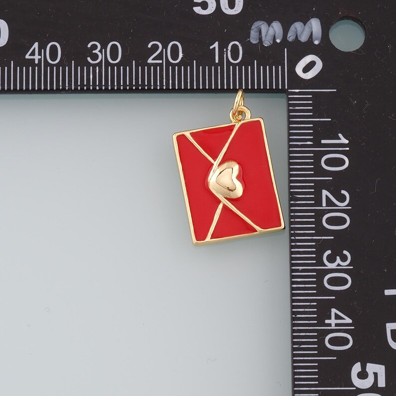 May include: Gold charm in the shape of a red envelope with a gold heart inside. The charm is approximately 2 cm wide.