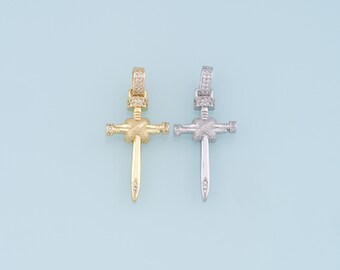 May include: Two pendant necklaces in the shape of a sword cross. One is gold-colored, the other is silver-colored. Both have a decorative bail and are encrusted with small, clear gemstones. The background is a light blue.