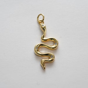Op de afbeelding: Een gouden slangenbedel met heldere kristallen accenten. De slang is opgerold in een spiraal met zijn staart omhoog.