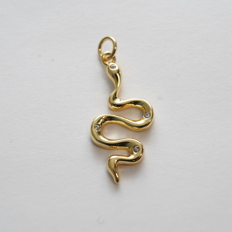Op de afbeelding: Een gouden slangenbedel met heldere kristallen accenten. De slang is opgerold in een spiraal met zijn staart omhoog.