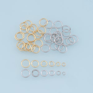 May include: A collection of gold and silver jump rings of various sizes. The jump rings are arranged in two groups, with the larger rings in the top group and the smaller rings in the bottom group.