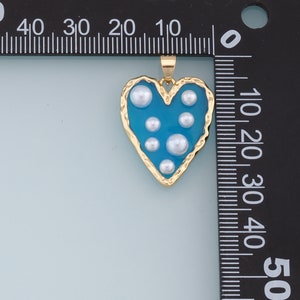 May include: A gold heart-shaped pendant with a blue enamel finish and white pearl accents.