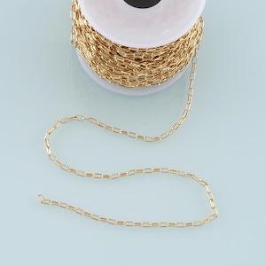 May include: A spool of gold-colored chain, with a portion of the chain uncoiled and lying on a light blue surface.