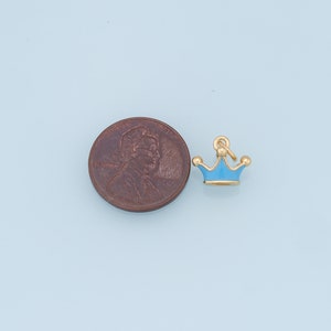 May include: A small blue and gold crown charm, shown next to a US penny for size comparison.