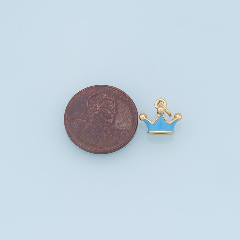 May include: A small blue and gold crown charm, shown next to a US penny for size comparison.