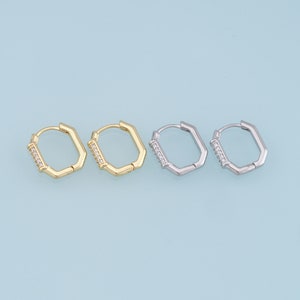 May include: Two pairs of hoop earrings, one pair is gold and the other is silver. Both pairs have a geometric shape and are adorned with small clear stones.