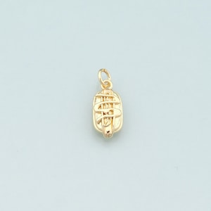 May include: A gold-colored pendant with a stylized design. The pendant has an oblong shape with intricate detailing, including curved lines and a small loop at the top for a chain. The overall design is symmetrical and ornate.