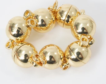 May include: A gold-colored bracelet composed of eight spherical, magnetic beads. Each bead is connected with a small loop and clasp. The bracelet has a shiny, reflective surface, and is set against a white background.