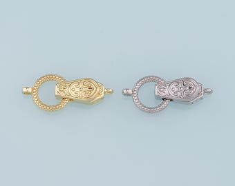 May include: Two ornate clasps for jewelry making, one gold and one silver. Each clasp has a round ring and a decorative, hinged, oval-shaped closure.