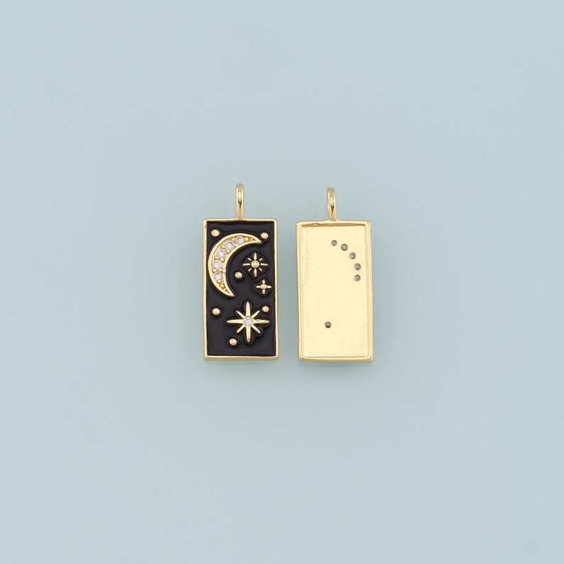 May include: Two gold-toned metal charms, one with a black enamel background and a crescent moon and star design with clear rhinestones, and the other with a plain gold background.