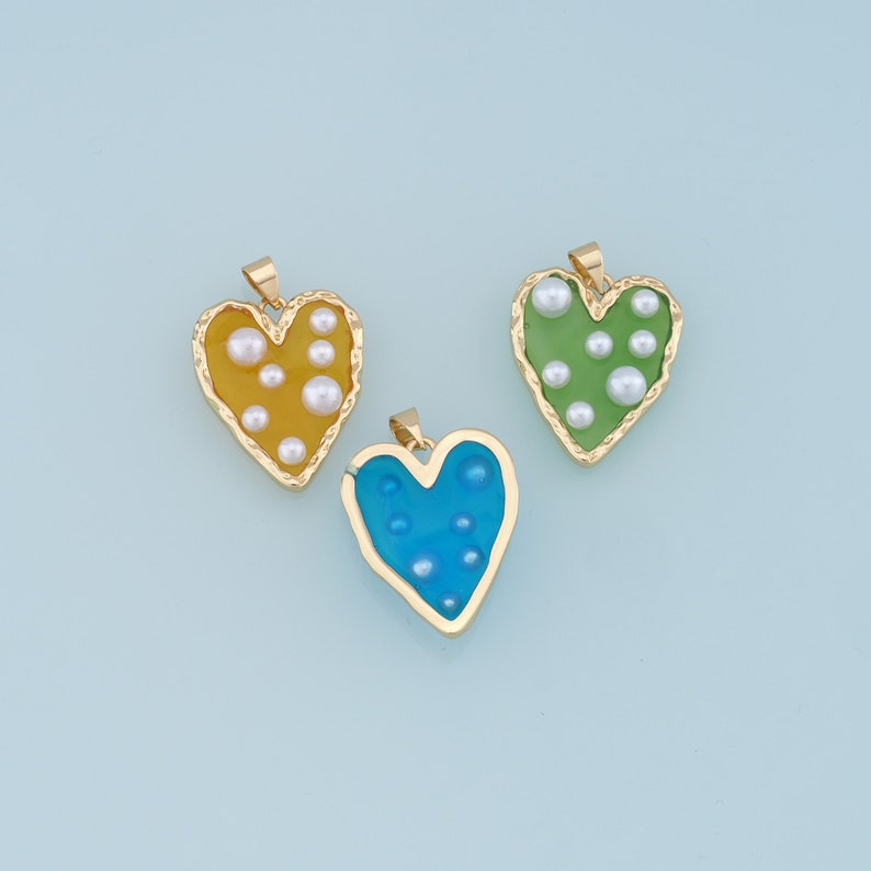 May include: Three gold heart-shaped pendants with different colored resin inserts and white pearl accents. The pendants are yellow, green, and blue.