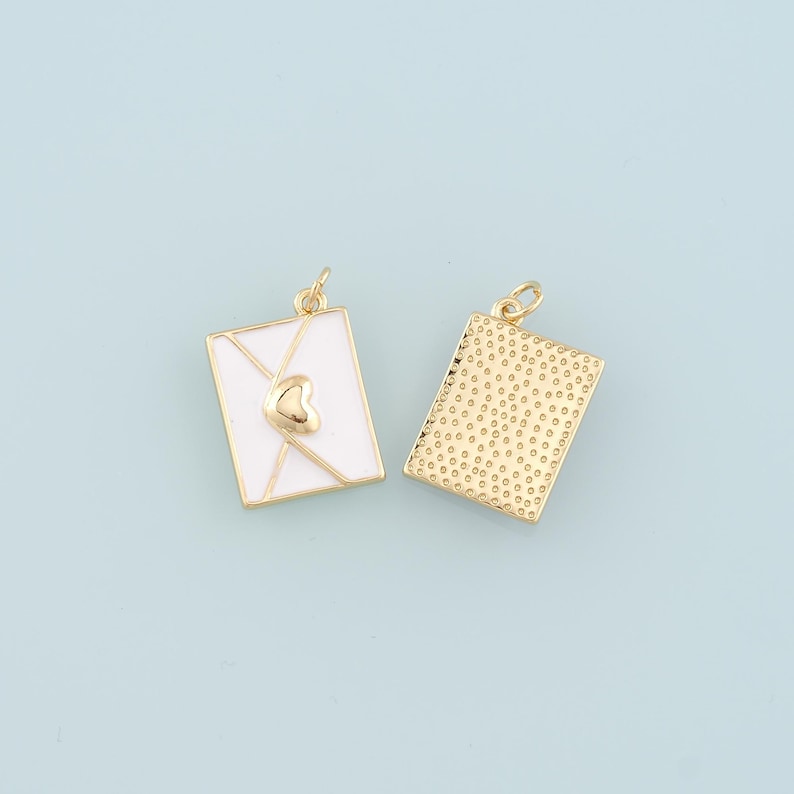 May include: Two gold-tone metal charms shaped like envelopes. One envelope charm is white enamel with a gold heart in the centre. The other envelope charm has a textured gold finish.