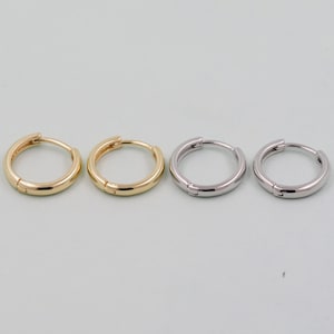 May include: Four hoop earrings, two gold and two silver, are arranged in a row on a light blue background.