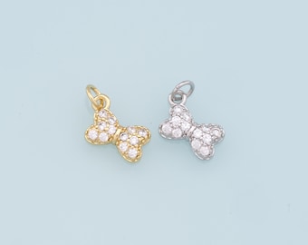 May include: Two gold and silver bow charms with clear crystal accents. The charms are in the shape of a bow with a loop at the top for attaching to a necklace or bracelet.