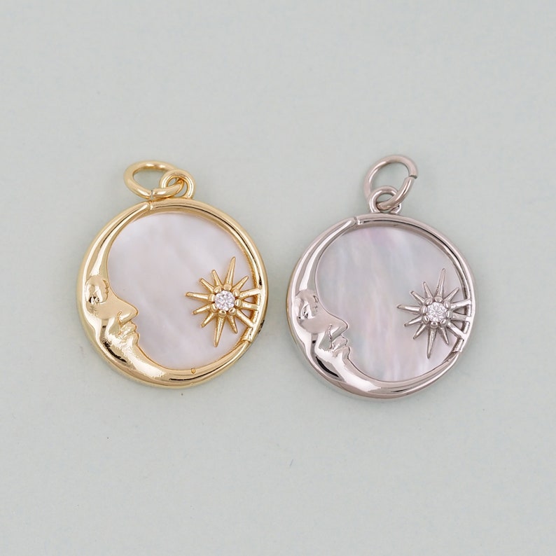 May include: Two crescent moon charms with a sun and a small crystal in the center. The charm on the left is gold and the charm on the right is silver.