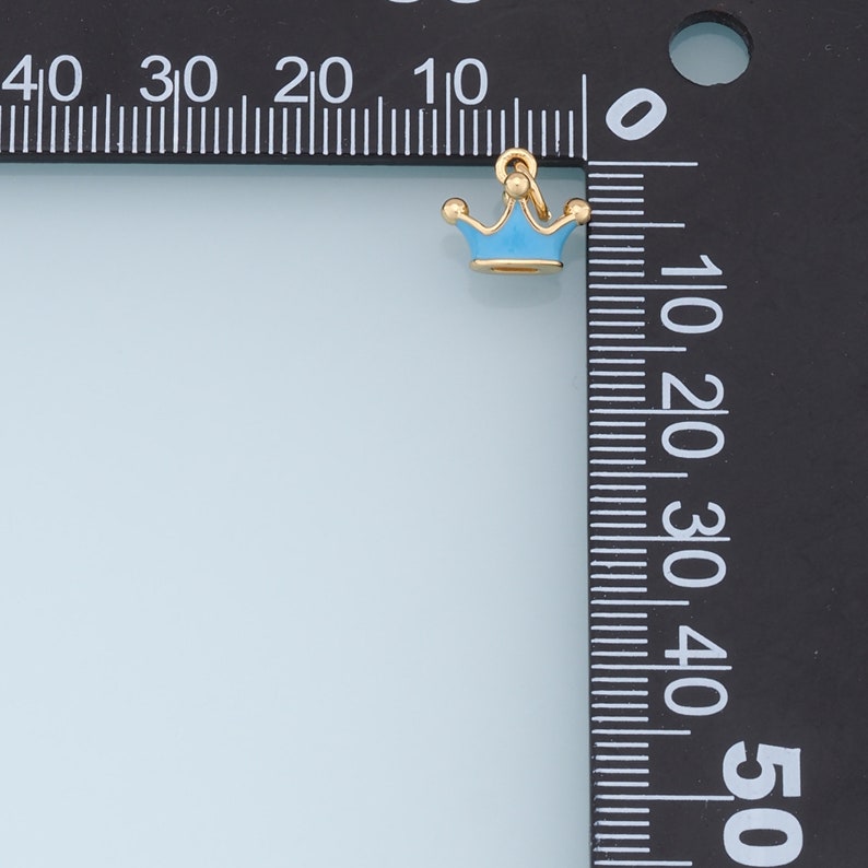 May include: A small gold crown charm with a light blue enamel finish. The charm is about 1 cm in size and has a loop for attaching to a necklace or bracelet.