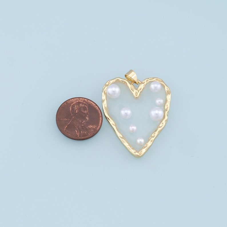 May include: Gold heart-shaped pendant with a clear resin center and white pearl accents.