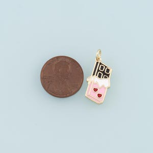 Pu&ograve; includere: Ciondolo dorato a forma di barretta di cioccolato con glassa rosa e bianca e cuori rossi. Il ciondolo &egrave; accanto a un centesimo di euro per il confronto delle dimensioni.
